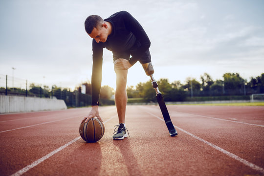 Full length of sporty caucasian handicapped man in sportswear and artificial leg dribble the ball while standing on racetrack.