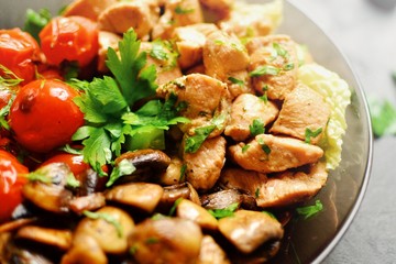 Tomatoes, chicken and mushrooms in a white plate on a dark background. Grilled tomatoes, fried champignons and grilled chicken. Vegetables and meat.
