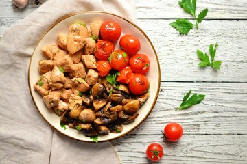 Tomatoes, chicken and mushrooms in a white plate on a light wooden background. Grilled tomatoes, fried champignons and grilled chicken. Vegetables and meat.