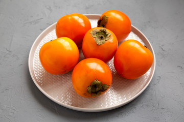 Raw Ripe Orange Persimmons on a plate over gray background, low angle view. Close-up.