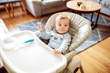 Fototapeta premium Beautiful caucasian hungry baby boy sitting in his chair and waiting for his mother to feed him.