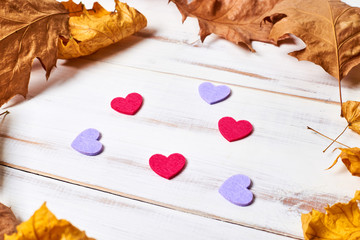 Frame of yellow autumn dry leaves and hearts on a white wooden background.