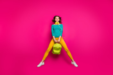 Full length body size photo of pretty sweet charming curly cute girlfriend wearing yellow pants trousers white footwear smiling toothily jumping up with rucksack isolated vivid fuchsia background
