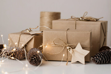 Three gifts Packed in Kraft paper and tied with rope. Decor-wooden star, cones, garland. On white background. Rustic style.