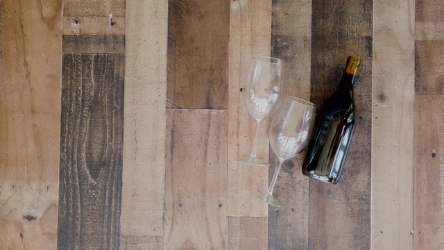 Two wine glasses roll into blank red wine bottle, on wood floor, flat lay, 4k.