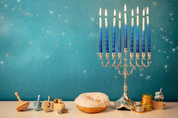 concept of of jewish religious holiday hanukkah with glittering raditional chandelier menorah, spinning top toys (dreidel), a doughnut and chocolate coins - obrazy, fototapety, plakaty