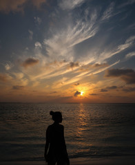 The young woman standing on the beach and can see beside only. In the evening, everything started to darken the the sky is golden light.The silhouette shot, Taken at Maafushi, Maldives Island