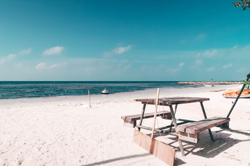An old wooden table type outdoor bench placed on the white sand beach. Background is deep blue and soft sea with 2-3 small boats parked. The clear sky not much clouds. Taken at Maldives, vintage tone.