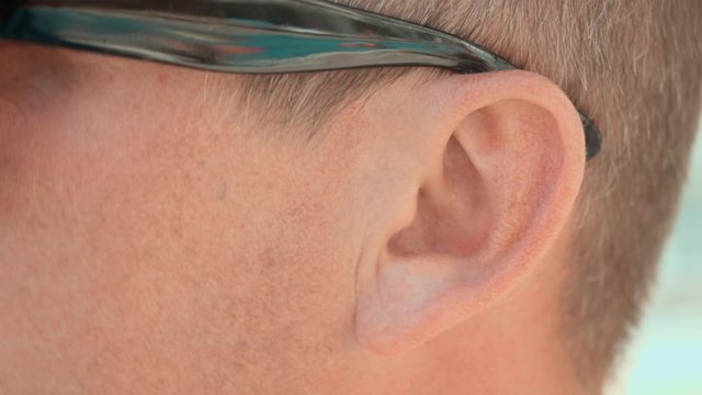 Close up male ear nodding man in sunglasses. Left ear of adult man wearing glasses and agreeing while conversation