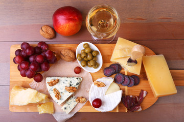 Assorted cheeses, nuts, grapes, fruits, smoked meat and a glass of wine on a serving table. Dark and Moody style. Free space for text.