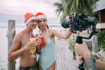 A young couple starred in a video with cocktails in Christmas caps on the ocean on a tropical island.