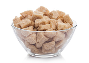 Glass bowl of natural brown unrefined sugar cubes on white background.