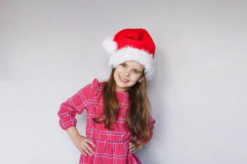 happy funny child girl in red Christmas hat on gray background.