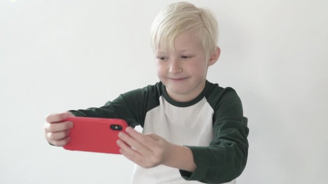 Blond boy makes selfie on the phone. A child photographs himself on a cell phone