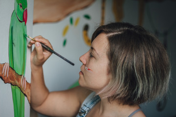 Young woman drawing a parrot on the wall in the. Woman decorating a children's room