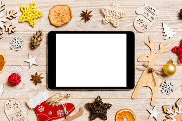 Top view of tablet on holiday wooden background. New Year decorations and toys. Christmas concept