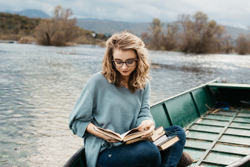 Portrait of young beautiful woman sitting on a boat and reading a book. She is bookworm and she...
