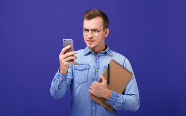 Teacher in denim shirt looking attentively on mobile phone attentively