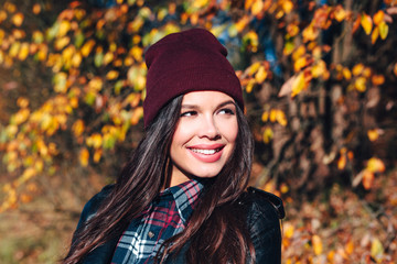 Stylish young woman in a hat and a plaid shirt in autumn park on a sunny day