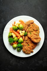 Chicken breast and vegetables. Chicken breast with carrots and brussels sprouts. Meat in a white plate on a dark background isolated. Horizontal view