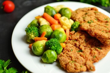 Chicken breast and vegetables. Baked chicken fillet, carrots, Brussels sprouts, broccoli, cauliflower. Food in a plate on a light wooden background. Close-up. Food on white plate 