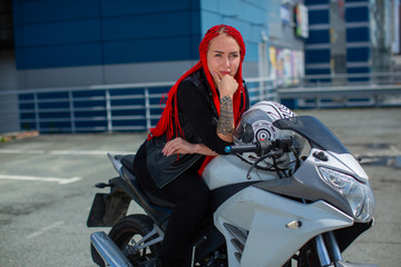 Fototapeta na wymiar Beauty with red hair sitting on a motorcycle in a thoughtful pose
