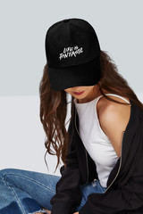 Cropped upward shot of a dark-haired girl, wearing black baseball cap with print with lettering...
