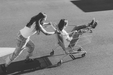 Black and white shot of Two happy hipster girls having fun with shopping cart outdoors