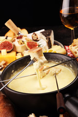 Gourmet Swiss fondue dinner on a winter evening with assorted cheeses on a board alongside a heated pot of cheese fondue with two forks dipping