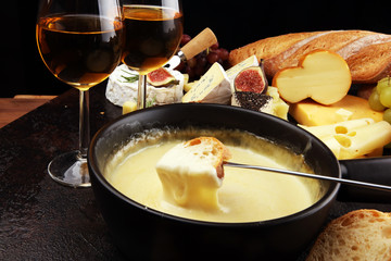 Gourmet Swiss fondue dinner on a winter evening with assorted cheeses on a board alongside a heated pot of cheese fondue with two forks dipping