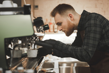 Сlose up portrait of bearded concentrated barista preparing cappuccino in a coffee shop. Cafe owner is focused on making coffee on a coffee machine, looks like coffee is poured into a cup