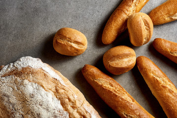 Fresh pastries. Baguettes, buns and wheat bread on a gray stone surface. Top view.