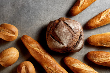 Obraz premium Fresh bakery. Baguettes, buns and rye bread on a gray stone surface. Top view.