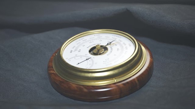 Brass barometer with wooden base on dark fabric close up