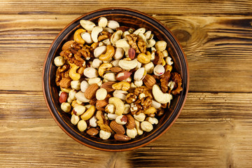 Mixed nuts on wooden table. Walnuts, pistachio, almond, peanut, cashew, hazelnut in ceramic bowl. Healthy eating concept. Top view