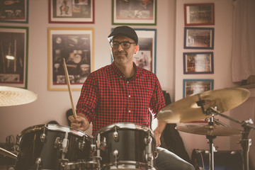 Caucasian young man with glasses and beret wearing a red and black plaid shirt, playing the drums...