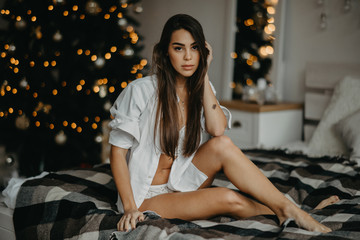 Fototapeta na wymiar Young woman sits on the bed against the background of the Christmas tree.