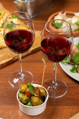 Two glasses of red wine with green olives on a table full of meals