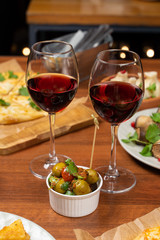 Two glasses of red wine with green olives on a table full of meals