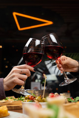 Clinking glasses of red wine above the table full of meals