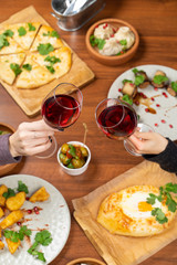 Clinking glasses of red wine above the table full of meals