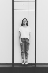 Black and white shot of young woman wearing white t-shirt and denim jeans is posing against the grey wall