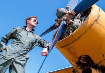 A handsome young pilot standing next to the propeller