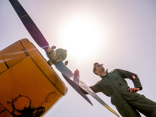 A handsome young pilot standing next to the propeller