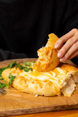 Woman is eating adjarian khachapuri with hands, crushing egg yolk