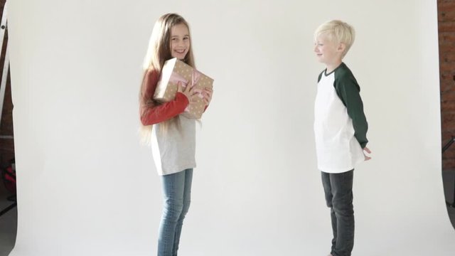 The boy gives the girl a gift. Happy girl hugs a friend and laughs merrily. Studio. White background. Youth bloggers