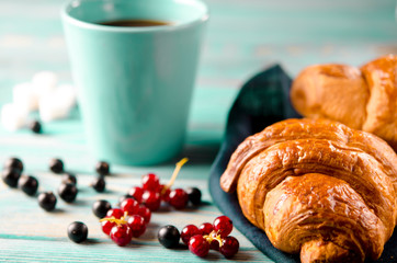 Fresh ruddy croissants with berries lie on a wooden table next to fresh black currant berries, red currants