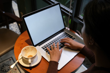 Obraz na płótnie Canvas A young girl working with a cup of cappuccino coffee with laptop white screen on table. Royalty high quality free stock photo image of woman typing, working on laptop with a coffee cup in coffee shop