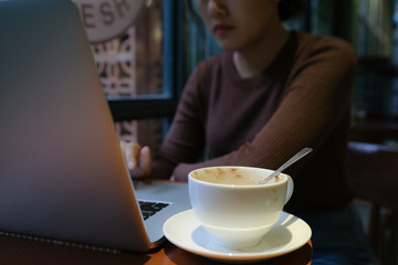 A young girl working with a cup of cappuccino coffee with laptop white screen on table. Royalty high quality free stock photo image of woman typing, working on laptop with a coffee cup in coffee shop