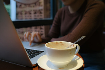 A young girl working with a cup of cappuccino coffee with laptop white screen on table. Royalty high quality free stock photo image of woman typing, working on laptop with a coffee cup in coffee shop